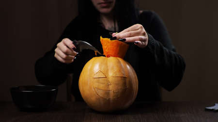 Young brunette woman carves a pumpkin for Halloween. Preparation for the holiday.の写真素材