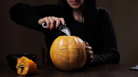 Young brunette woman carves a pumpkin for Halloween. Preparation for the holiday.の写真素材