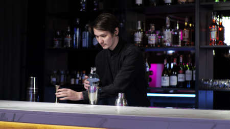 Young novice bartender trainee preparing a cocktail Careless guy Mixes drink and ice in a shaker