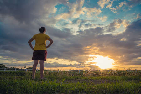 Beautiful woman on green meadow watching the sunset ray light and dramatic clouds in summer