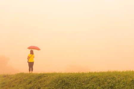 Woman alone in fog with pink umbrellaの写真素材