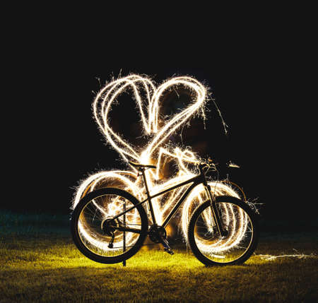 Silhouette of mountain bicycle on Green meadow with Beautiful Fireworks sparkler heart symbol at...