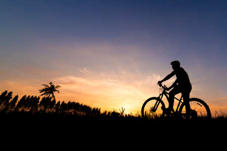 Silhouette man with mountain bicycle at sunsetの写真素材