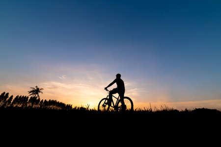 Silhouette man with mountain bicycle at sunsetの写真素材