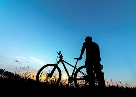 Silhouette man with mountain bicycle at sunsetの写真素材