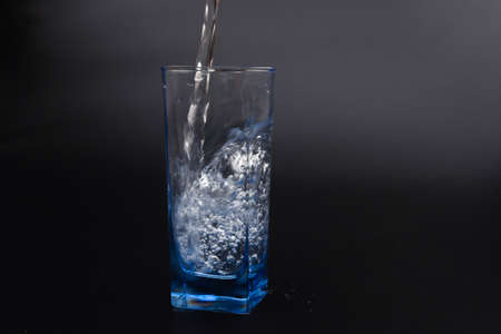 pouring fresh drink water to blue glass on black backgroundの写真素材