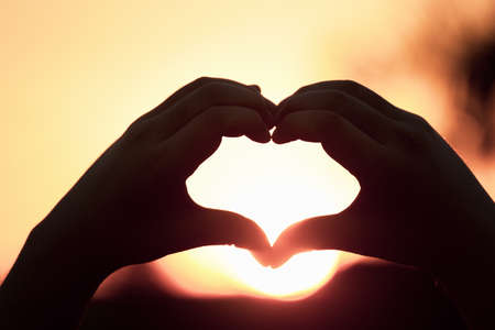 Beautiful Silhouette hand made heart shape on the sunset background.