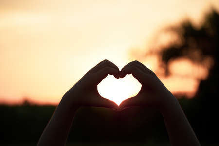 Beautiful Silhouette hand made heart shape on the sunset background.の写真素材