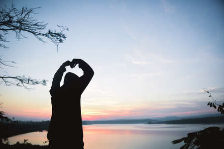 Man making Hands in Heart Shape on Silhouette sky Background.の写真素材