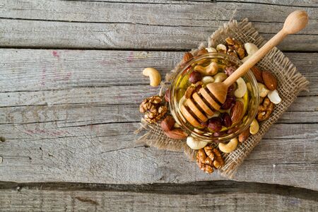 Honey in glass jar and dipper, selection of nuts  on rustic wood backgroundの写真素材