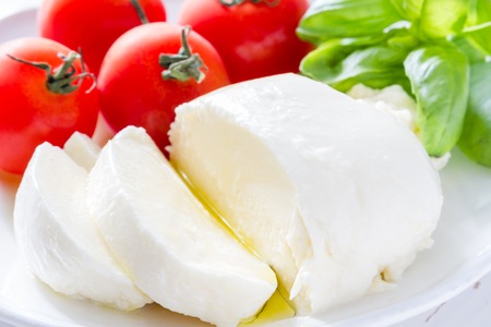 Tomato mazzarella, basil on white plate, white wood backgroundの写真素材
