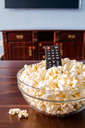 Popcorn in glass bowl and remote control on wood backgroundの写真素材
