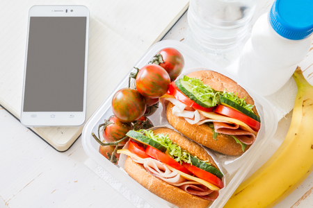 Lunch box with yogurt and berry, phone and notepad, white wood background, closeupの写真素材