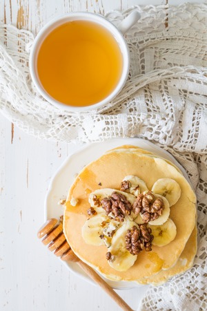 Pancakes with banana, nuts and honey, white wood background, top viewの写真素材