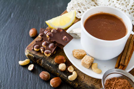 Hot chocolate in white cup, selection of chocolate and nuts, dark stone background, copy space
