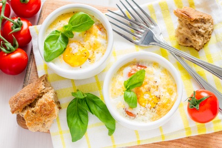 Egg cocotte  in white ramekin with tomato and basil, white backgroundの写真素材