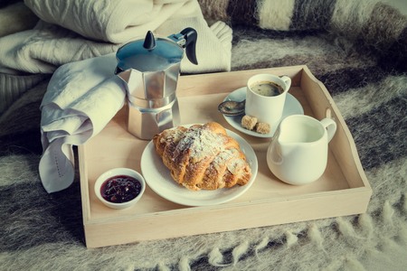 Breakfast in bed - coffee, croissant, milk on tray, wool blanket, tonedの写真素材