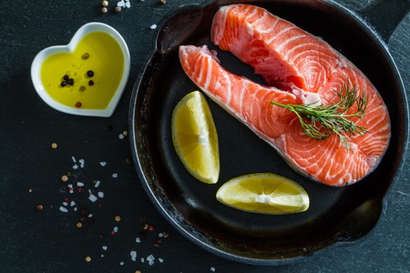 Salmon steak with lemon slices and spices, dark stone background, top viewの写真素材