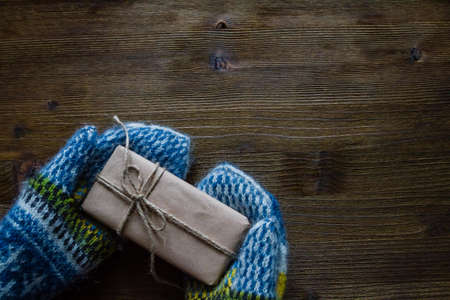 Hand in knitted mittens holding present, rustic wood background, top view, copy spaceの写真素材