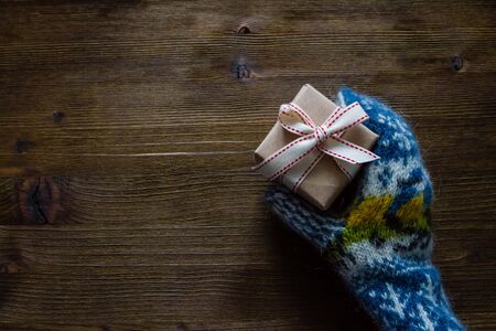 Hand in knitted mittens holding present, rustic wood background, top view, copy space