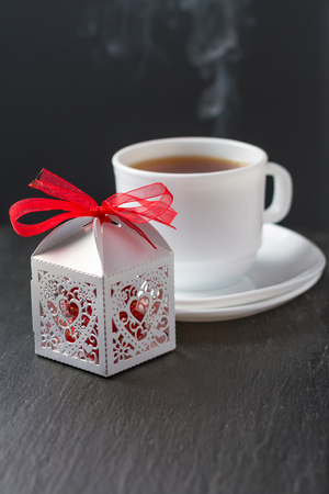 Present in white box and hot steaming tea, dark background, copy spaceの写真素材