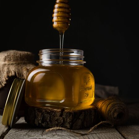 Golden honey in glass jar with dipper, dark photoの写真素材