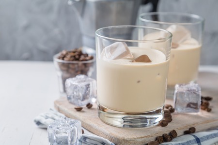 Coffee liqueur in glasses with ice and beans, wood background, copy space