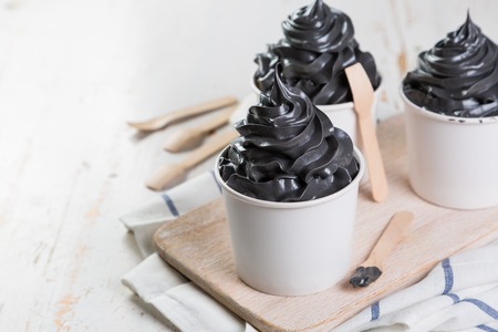 Black ice cream in white cups on rustic wood backgroundの写真素材