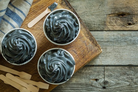 Black ice cream in white cups on rustic wood backgroundの写真素材