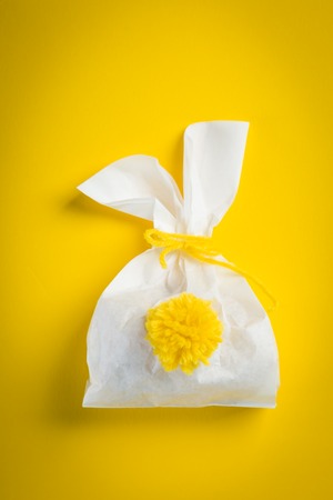 Easter concept - bunny shaped bag with eggs and flowers on bright yellow background,