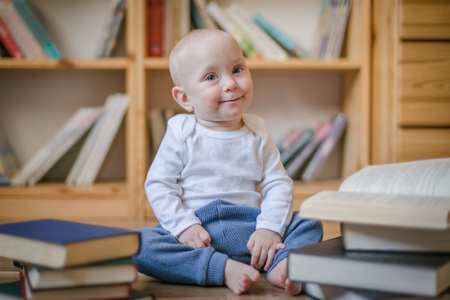 Toddler girl sitting with books in front of book shelvesの写真素材