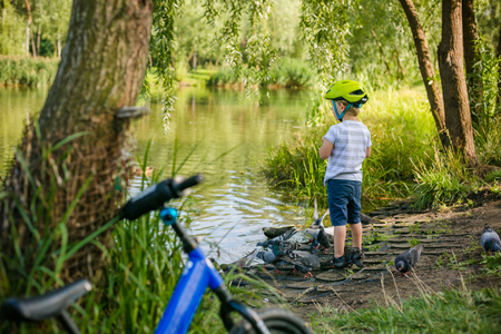Boy feeding ducks and pigeons in the park by the lakeの写真素材