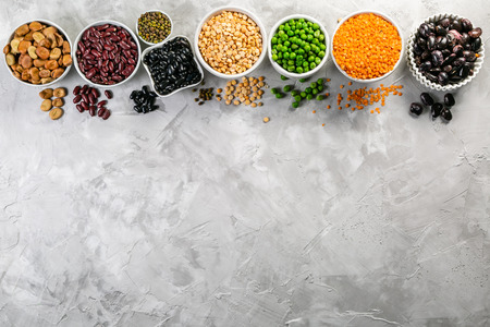 Selection of legumes in white bowls on stone background