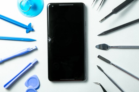 Broken phone with tools for repair, service concept