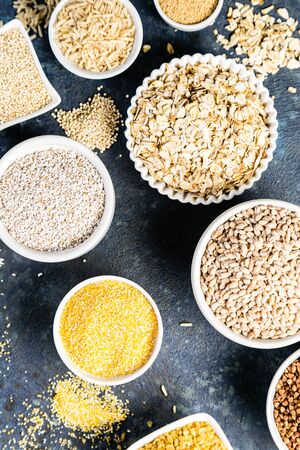 Selection of whole grains in white bowls - rice, oats, buckwheat, bulgur, porridge, barley, quinoa, amaranthの写真素材