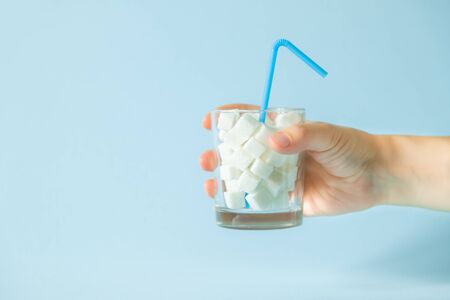 Excessive sugar consumption concept - hand holding glass with sugar cubesの写真素材