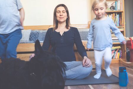 Mother doing yoga, calm and relaxed while kids and dog run around making noiseの写真素材
