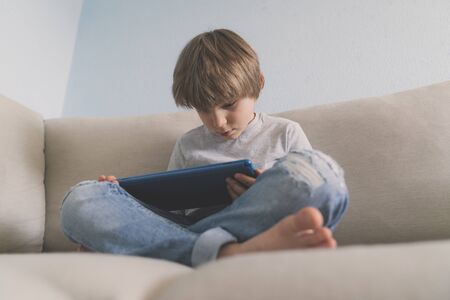 Young boy usina tablet on sofa at homeの写真素材
