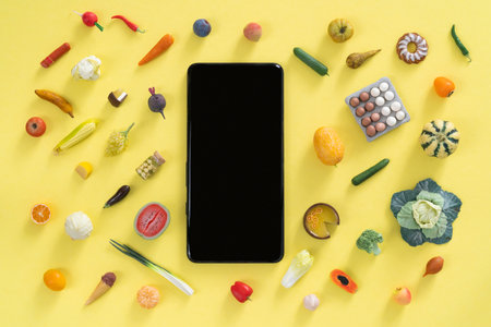 Online shopping concept - different foods and phone on yellow backgroundの写真素材