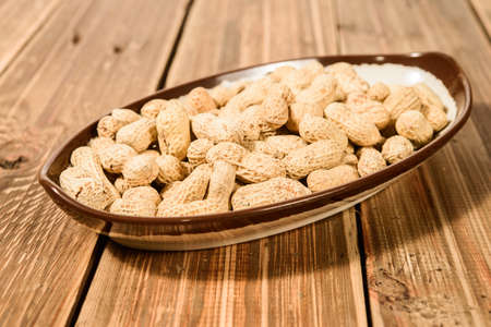 Bowl with peanuts on wood background
