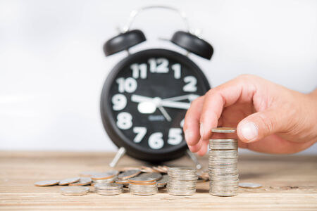 Antique clock and Hand stacking up Thai coinsの写真素材