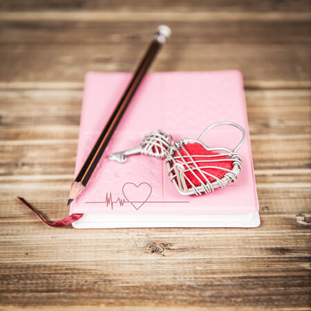 Pink love diary and red heart on wood backgroundの写真素材