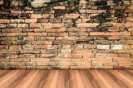 Grungy textured red brick and stone wall with warm brown wooden floor inside old neglected and...