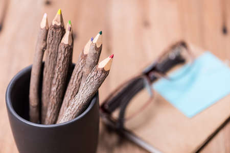 color pencil made of branches in cup with glasses and note book on wood backgroundの写真素材