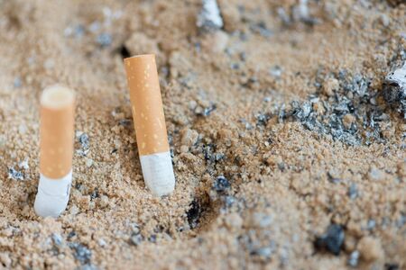 close up Smoked cigarettes in a dirty ashtray with sand.