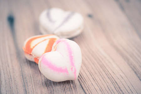 A lot of french colorful macarons in heart shape on a woody floor in vintage tone styleの写真素材