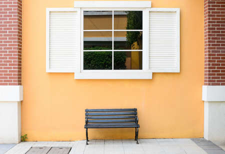 sidewalk scene with wooden bench and orange wall and windowの写真素材