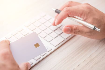 hand holding a white credit card and typing. On-line shopping on the internet