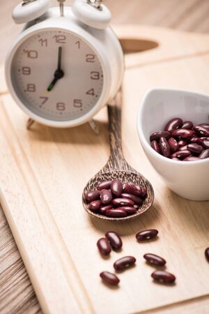 red beans in ceramic bowl with alarm clock on wood backgroundの写真素材