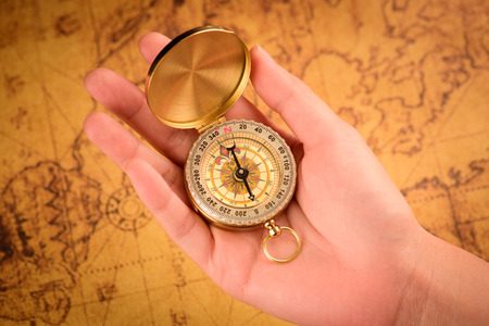 Close up of the hand holding a vintage compass over a vintage map